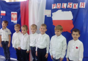 Grupka chłopców pozuje do zdjęcia na tle patriotycznej dekoracji.